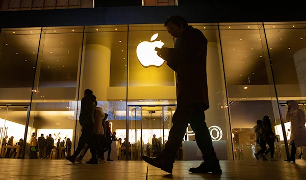 file photo, a man looks at his phone as he walks past a store of U.S. tech giant Apple in a retail district in Beijing on December 13, 2024