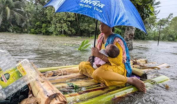 A woman and her child wade through floodwaters in Feni, one of the worst-hit areas, on August 23, 2024. (AFP)