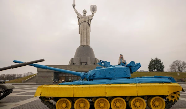 A child plays on a tank painted in the colors of the Ukrainian flag, back dropped by the Motherland Monument, in Kyiv, Ukraine, Friday, March 15, 2024. (AP)