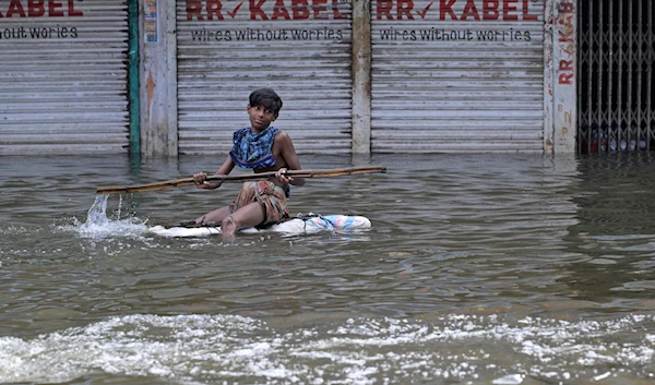 A young boy uses a bamboo to steer himself floating on a log of wood through a flooded street in Feni, a coastal district in southeast Bangladesh, Saturday, Aug. 24, 2024. (AP)