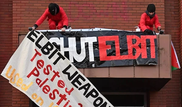 Activists from Extinction Rebellion North and Palestine Action fix a banner as they protest outside the Elbit Ferranti factory in Oldham, in northwest England, on February 1, 2021. (AFP)