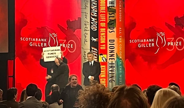 A protester holding a sign saying ‘Scotiabank Funds Genocide’ is escorted off the stage during the Scotiabank Giller prizegiving in Toronto, on November 13, 2023. (AP)