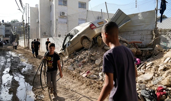 Palestinian refugees walk past a damaged vehicle in the West Bank refugee camp of Tulkarem during an Israeli incursion into Tulkarem, Thursday, September 12, 2024 (AP)