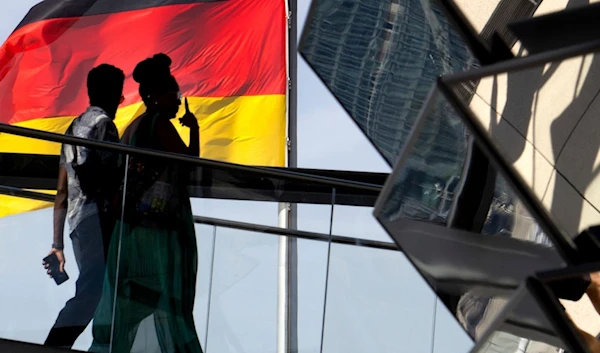 Two people walk in front of a German national flag as they visit the dome of the Reichstag building, home of the German federal parliament, Bundestag, in Berlin, Germany, September 1, 2024 (AP)