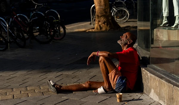 An Israeli settler sits on the sidewalk next to a mall in Tel Aviv, occupied Palestine, Thursday, Aug. 15, 2024. (AP)