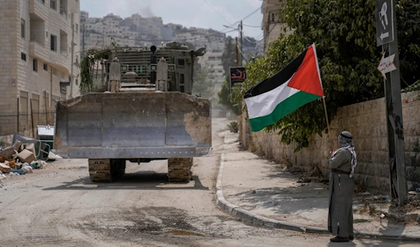 A man waves the Palestinian flag as a convoy of Israeli military bulldozers drive by during an occupation raid in Jenin, West Bank, Monday, Sept. 2, 2024. (AP)