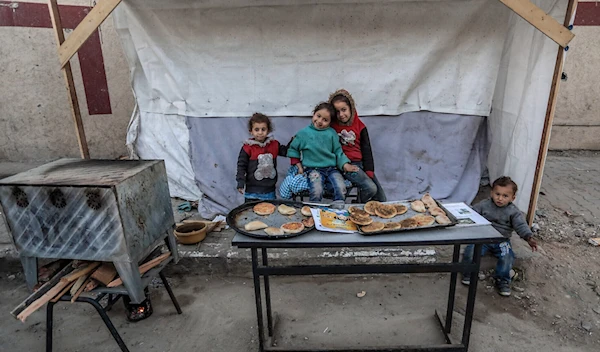 Palestinian Children pose for a picture at a stand selling flatbread in Deir al-Balah in central Gaza on March 3, 2024 amid Israeli genocide. (AFP)