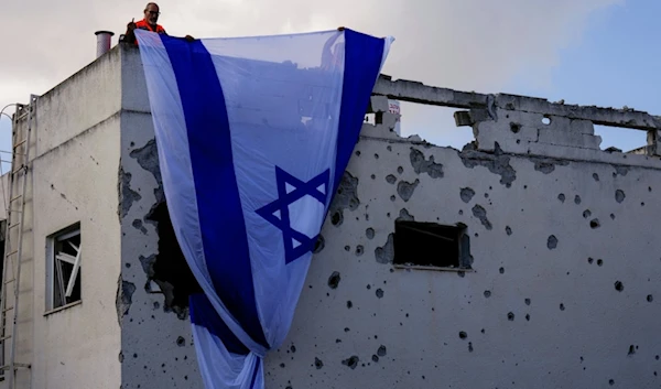 Municipality workers hang an Israeli flag over a damaged building that was hit by a rocket fired from Lebanon, in Kiryat Bialik, northern occupied Palestine, on Sunday, September 22, 2024 (AP)