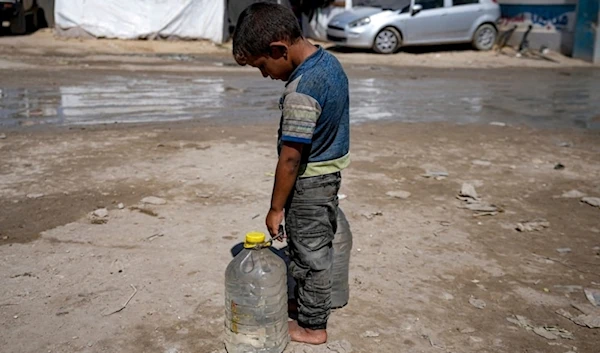 A displaced child carries filled water bottles at a makeshift tent camp in Deir al-Balah, central Gaza Strip, Thursday, August 29, 2024. (AP)