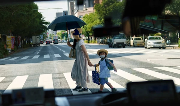 A pedestrian crossing a street with a child is seen through a taxi window in Tokyo, Monday, July 19, 2021 (AP Photo/David Goldman, File)