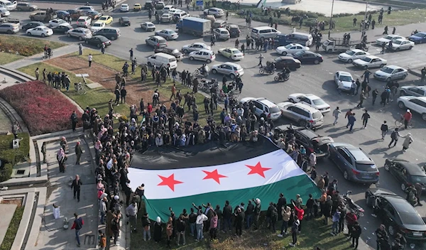 People celebrate holding a large Syrian opposition flag at Umayyad Square in Damascus on December 9, 2024. (AFP)