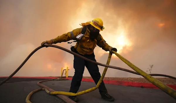 A firefighter sets out fire hoses to fight the Hughes Fire. (AP)